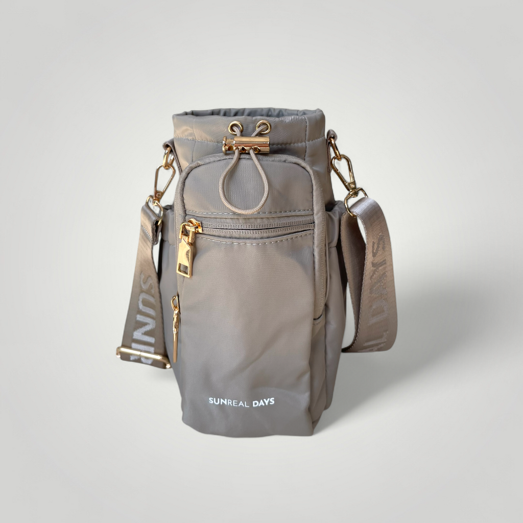 Dune water bottle carry bag with gold accents and 'Sunreal Days' branding. Zipped pockets to hold phone and keys.