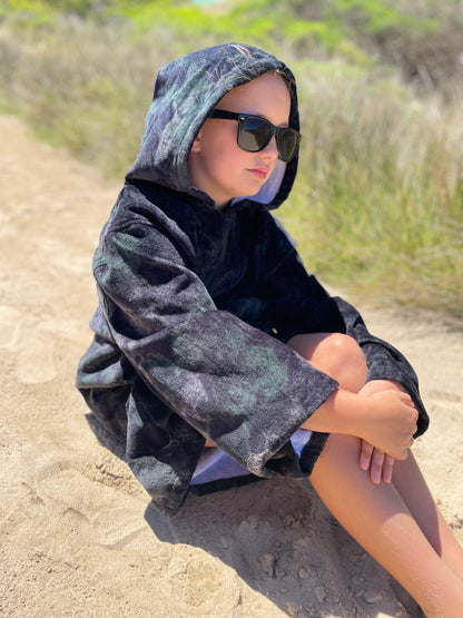 Child sitting on beach wearing sunreal days black hooded towel
