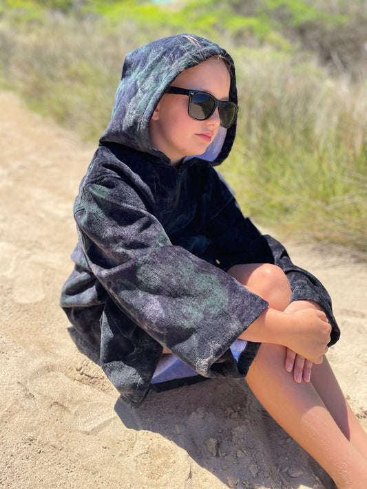 Child sitting on beach wearing sunreal days black hooded towel